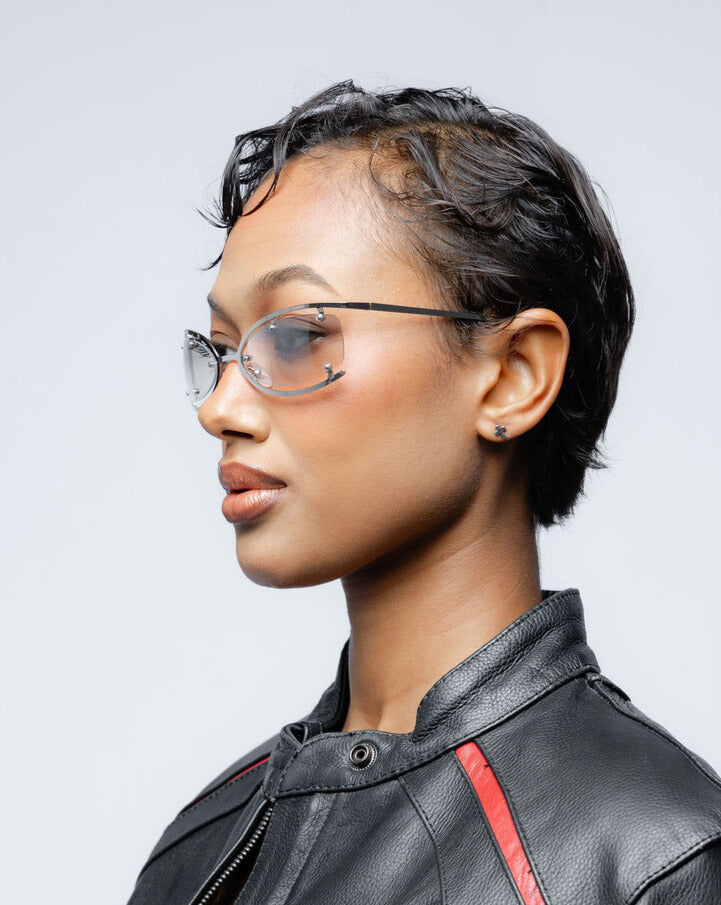 Woman wearing silver metal frame glasses and a black leather jacket with red accents against a light gray background