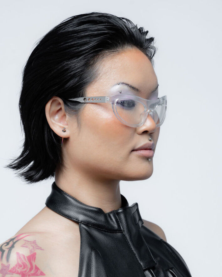 Person wearing clear glasses and a black leather outfit against a light gray background