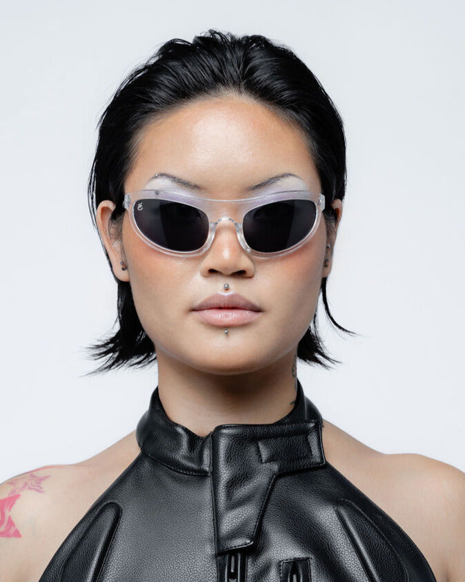 Person wearing black sunglasses and a black outfit against a light gray background