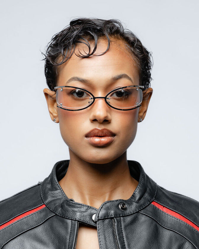 Woman wearing silver metal frame glasses and a black leather jacket with red accents against a gray background