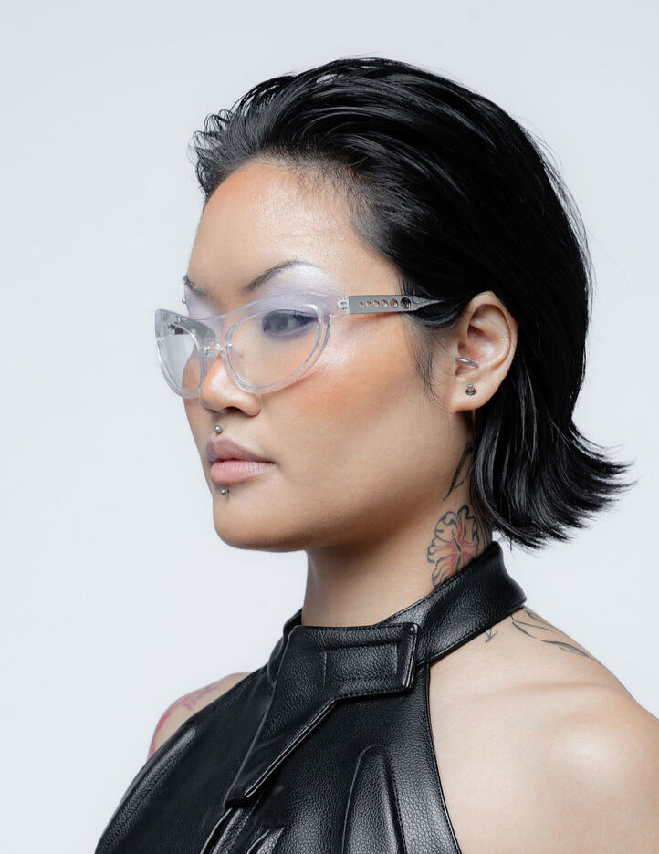 Person with stylish haircut and glasses wearing a black outfit against a light background